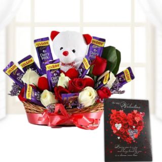 Beautiful basket arrangement of teddy bear sitting in basket of red and white roses with dairy milk chocolates, and a valentine day greeting card