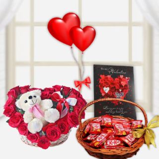 cute teddybear sitting in a heart shape arrangement of red roses with basket of kitkat chocolates, 2 heart shape balloons, and a valentine day greeting card 